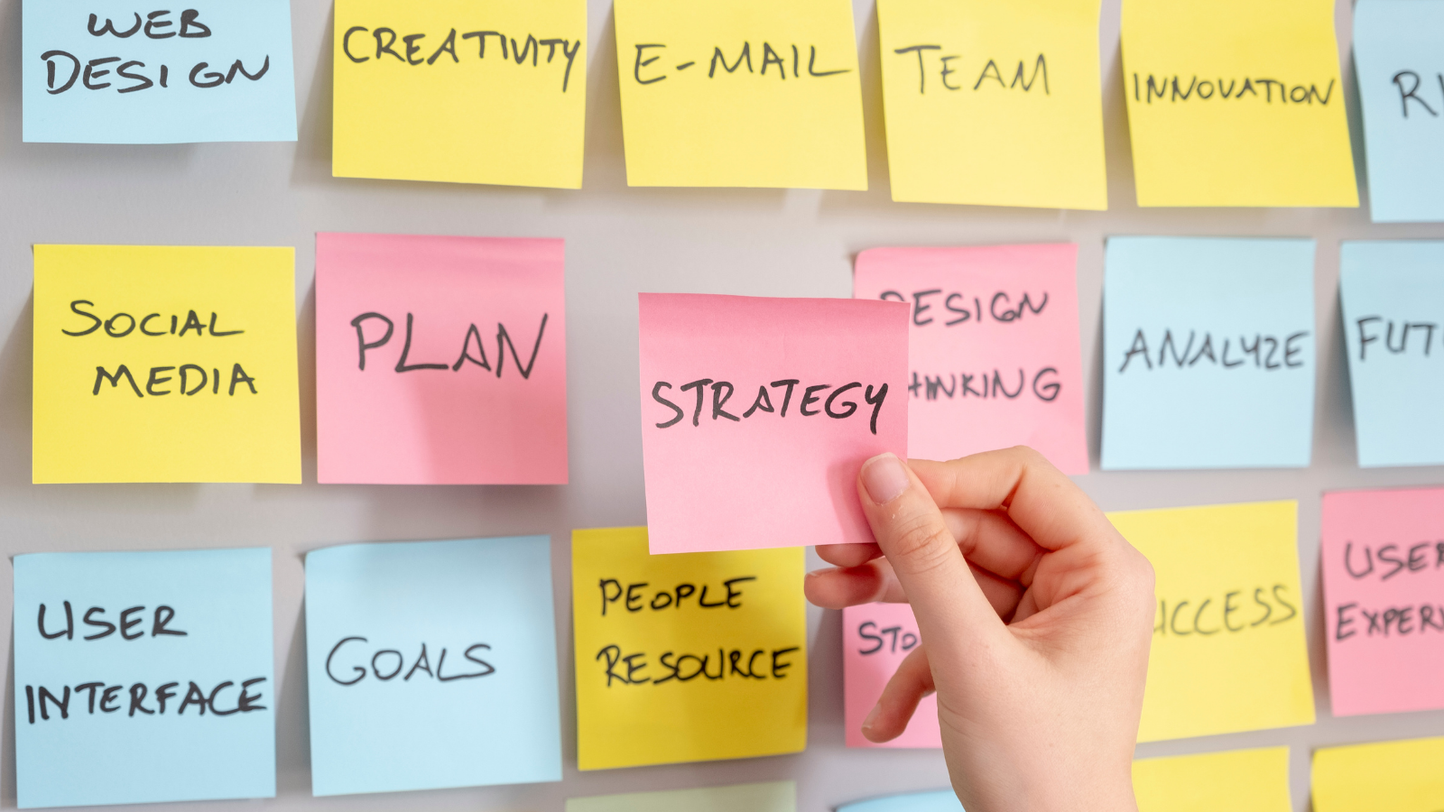 multi-colored sticky notes with marketing terms and a hand holding one that reads,
